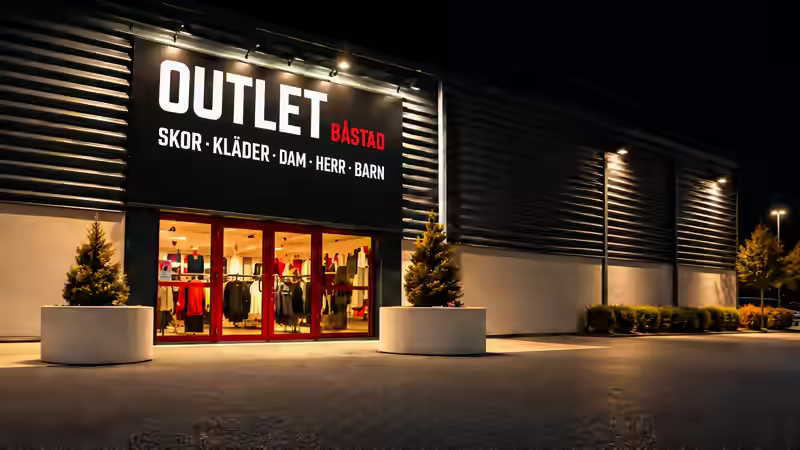 Outlet Båstads fasad och entré med upplyst skylt i kvällsljus
